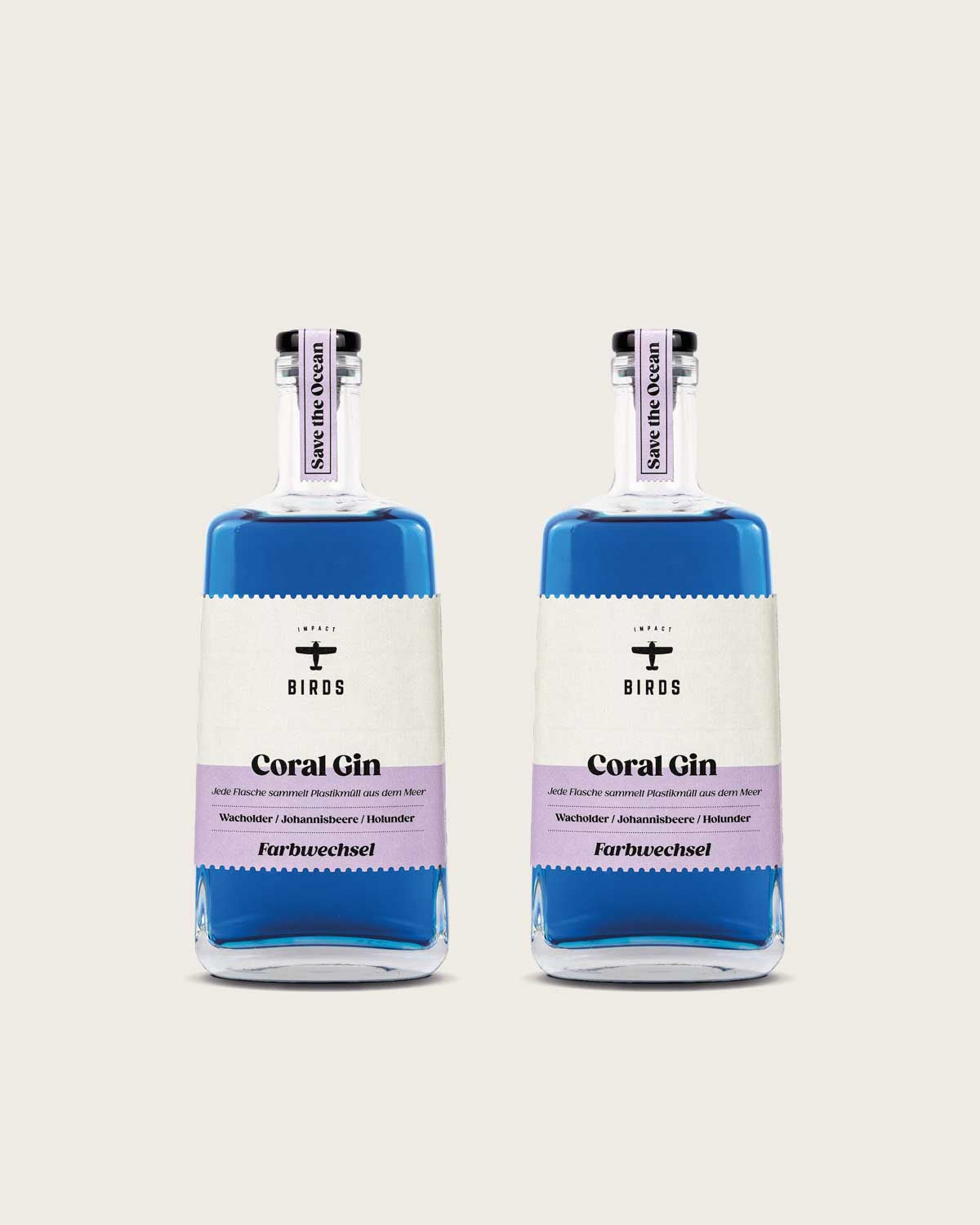 Zu sehen sind zwei Flaschen unseres Coral Gin, der Farbwechsel Gin mit Impact. Es handelt sich um zwei Glasflaschen, die blaue Farbe des Gins ist deutlich zu sehen. Das Etikett ist stilvoll in einem beige und lila gefärbt.